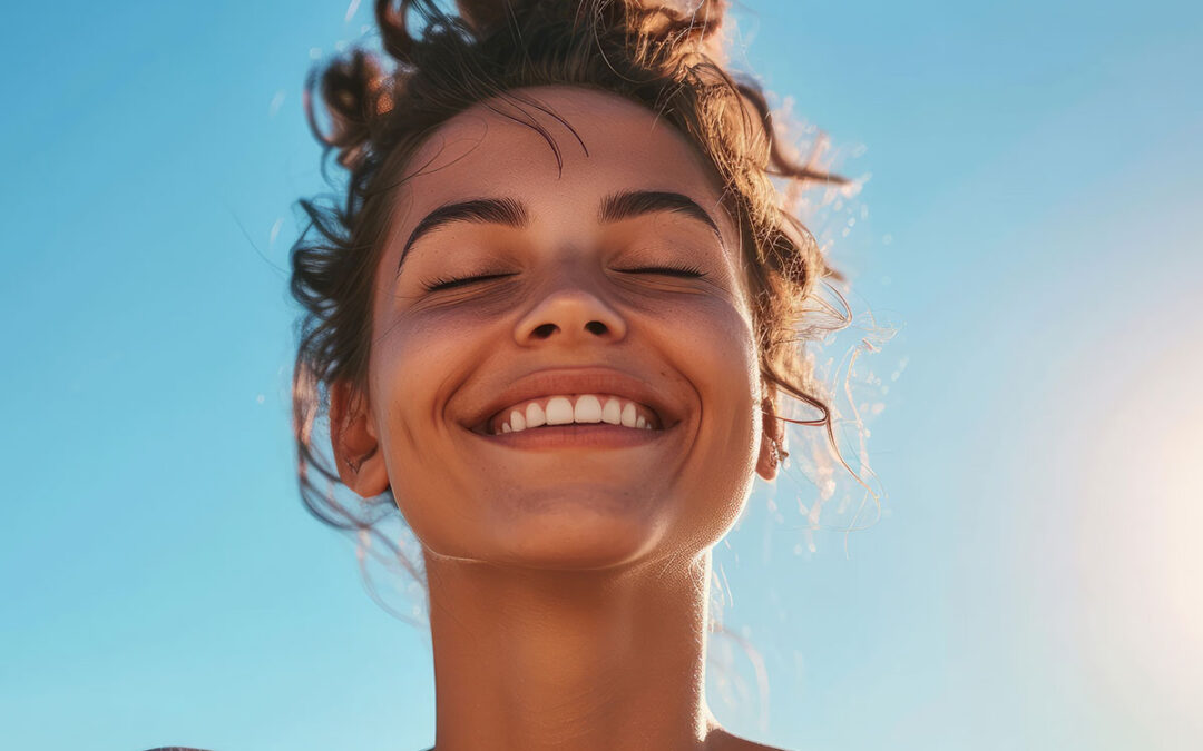 Fit young woman smiles while deep breathing in front of a clear blue sky on a sunny and windy summer day