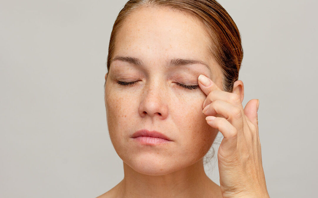 Middle aged caucasian woman of 40s with closed eyes holding finger on eyelid to show eyes aging