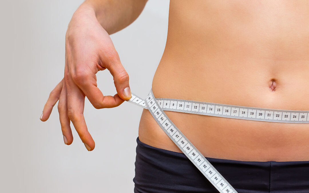 Young woman measuring her waistline in a gym with a tape