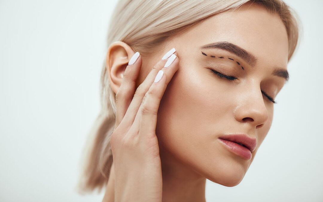 Beautiful young blonde woman keeping eyes closed and touching her face with sketch on it
